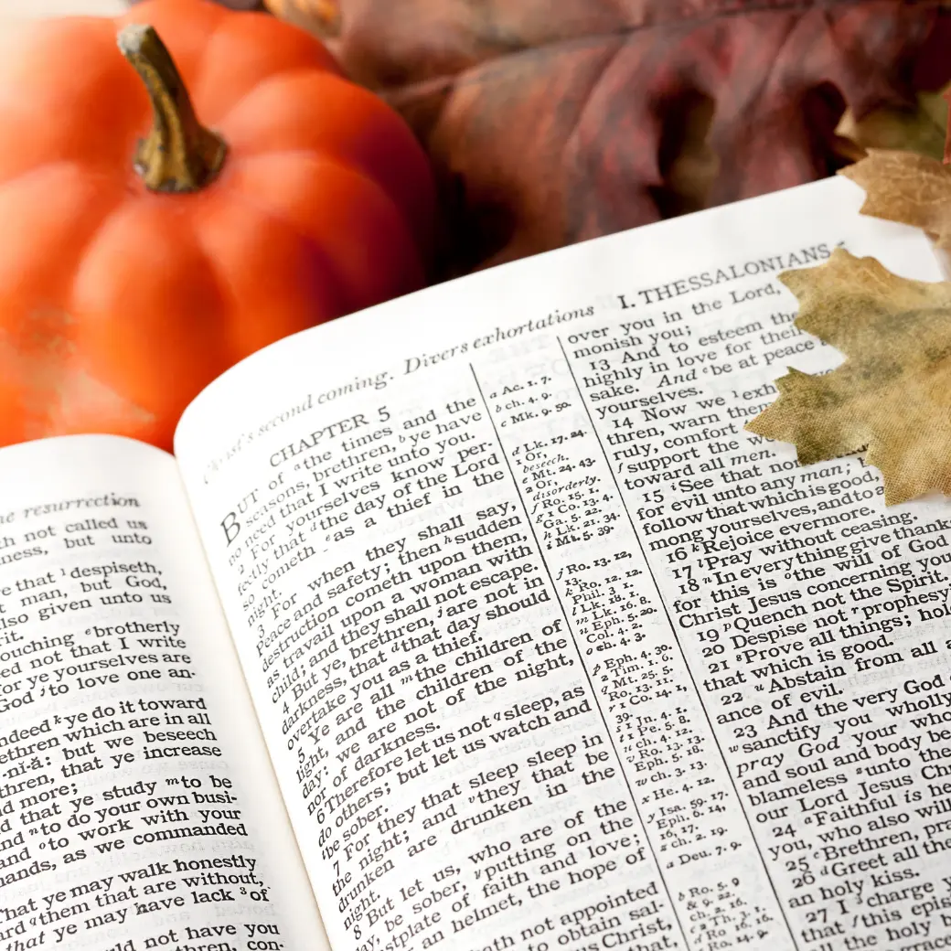An open Bible turned to 1 Thessalonians beside a small pumpkin and autumn leaves